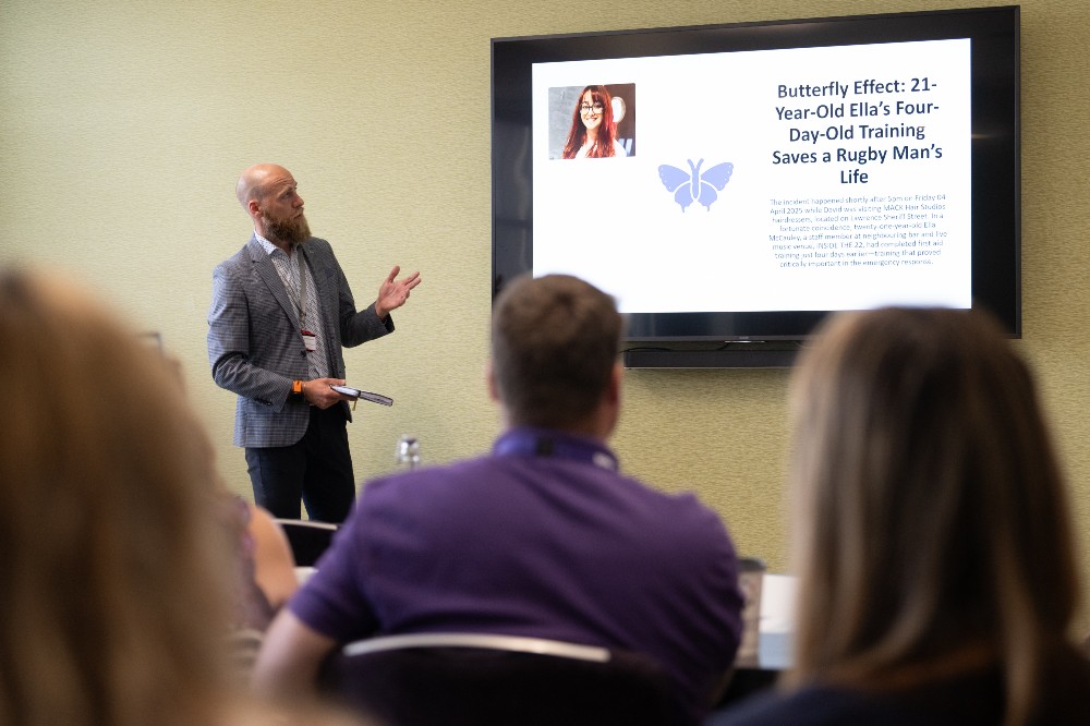 Person stood at the front of a wellbeing forum event giving a talk