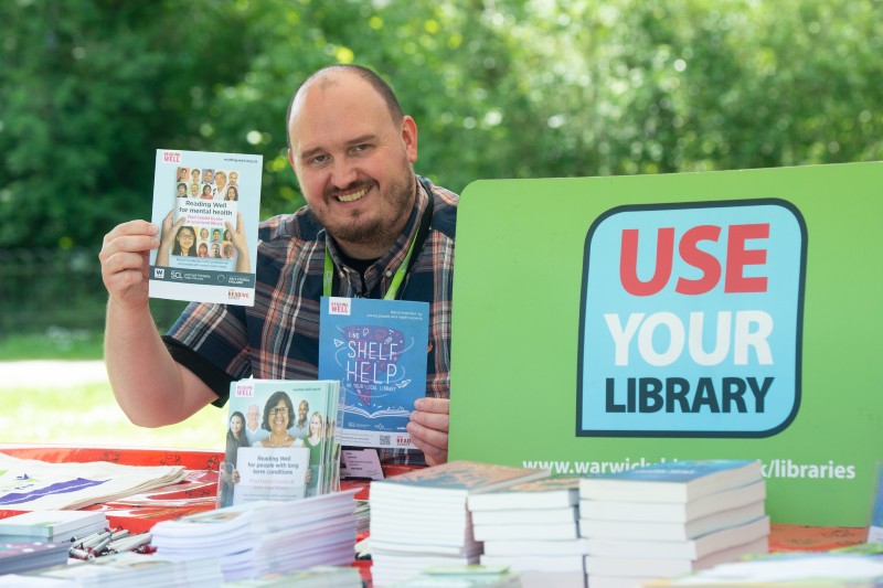 Man sat at stall with sign for use your library.