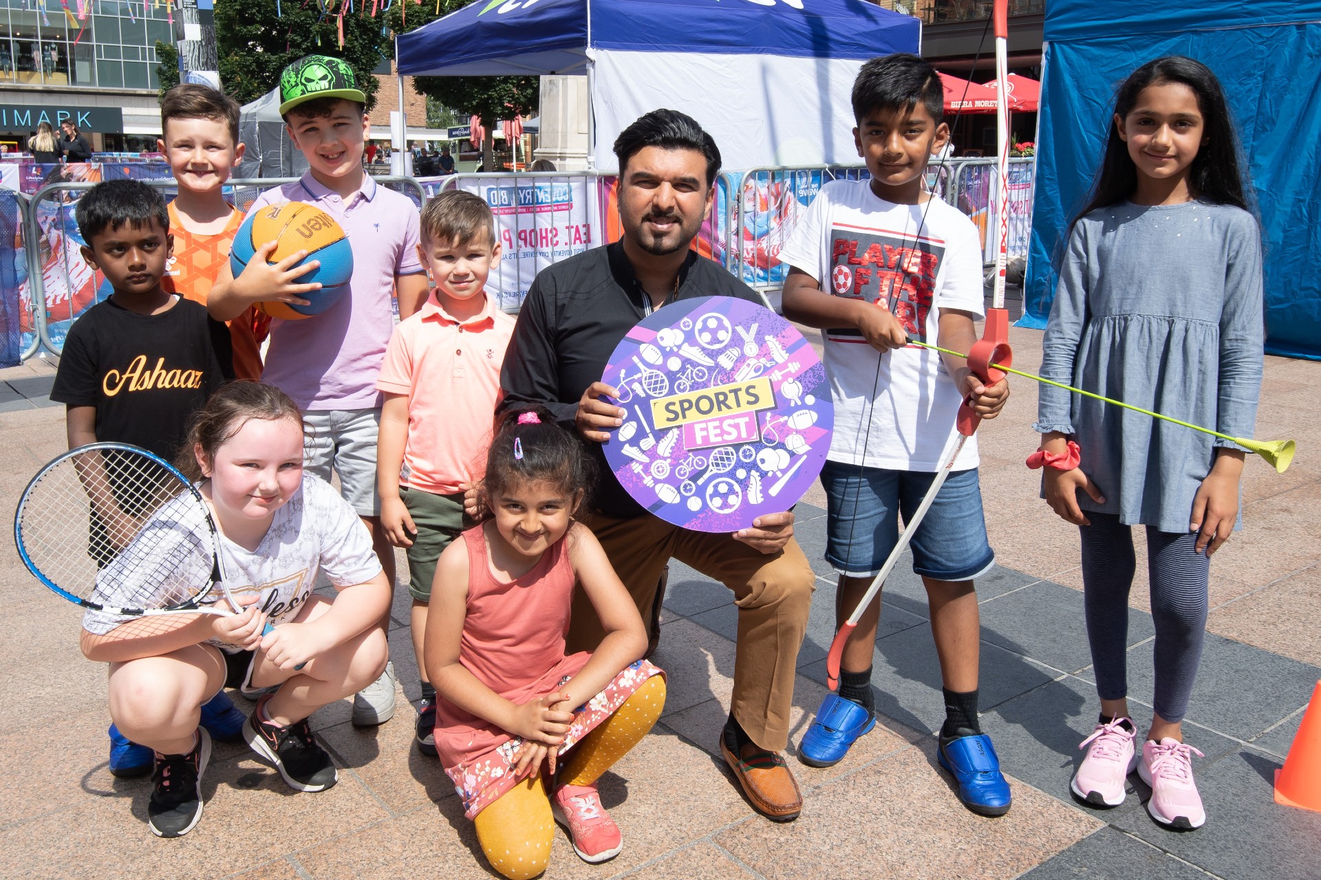 Adult with group of children, several holding various items of sports equipment